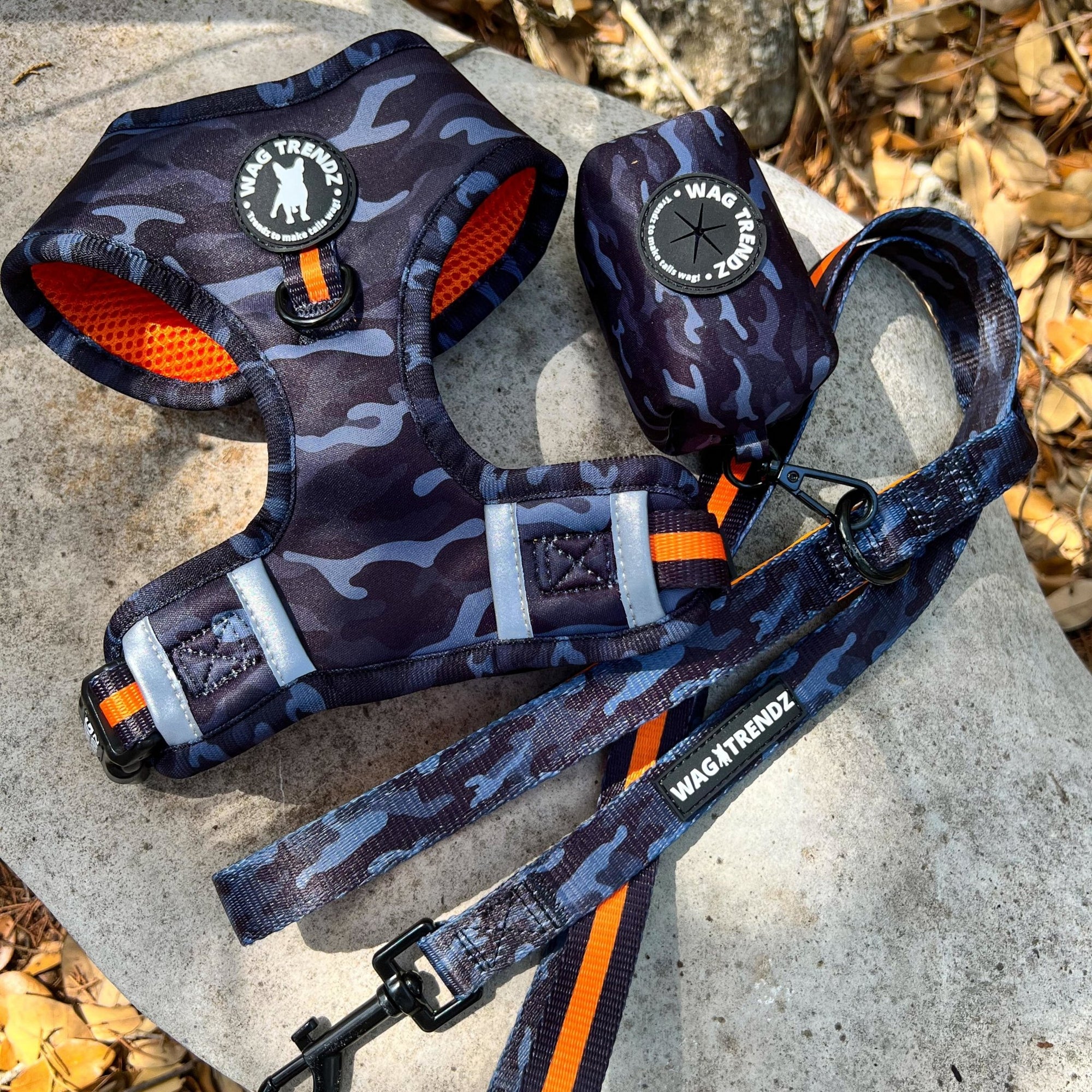 No Pull Dog Harness - black and gray camo with orange accents on dog adjustable harness vest with front clip - chest side view - matching dog leash and poop bag holder - laying outdoors in the sun on a rock  - Wag Trendz
