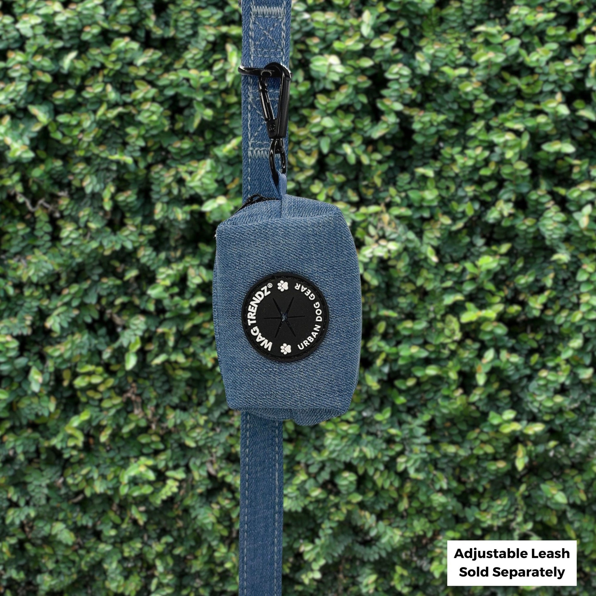 Dog Poop Bag Holder - Downtown Denim - hanging on a denim dog leash with the black rubber logo dispenser on front - against a greenery background - Wag Trendz