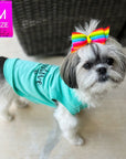 Dog T-Shirt - Shih Tzu mix wearing "Stay Pawsitive" teal dog t-shirt - with "Stay Pawsitive" lettering in black on back and a paw print emoji in black on chest - standing outdoors on a patio and wearing a colorful bow in her hair  - Wag Trendz