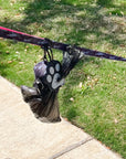 Poop Buddy - black and gray resin dog paw - hanging on a dog leash - outdoors with grass and sidewalk in background - Wag Trendz