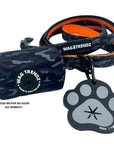 Poop Buddy - black and gray resin dog paw - attached to a black and gray camo leash with orange accents and camo poop bag holder - against white background - Wag Trendz