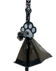 Poop Buddy - black and gray resin dog paw - hanging on a black & white XO dog leash with red accents and black plastic bag carrying poop pushed through hole - against white background - Wag Trendz