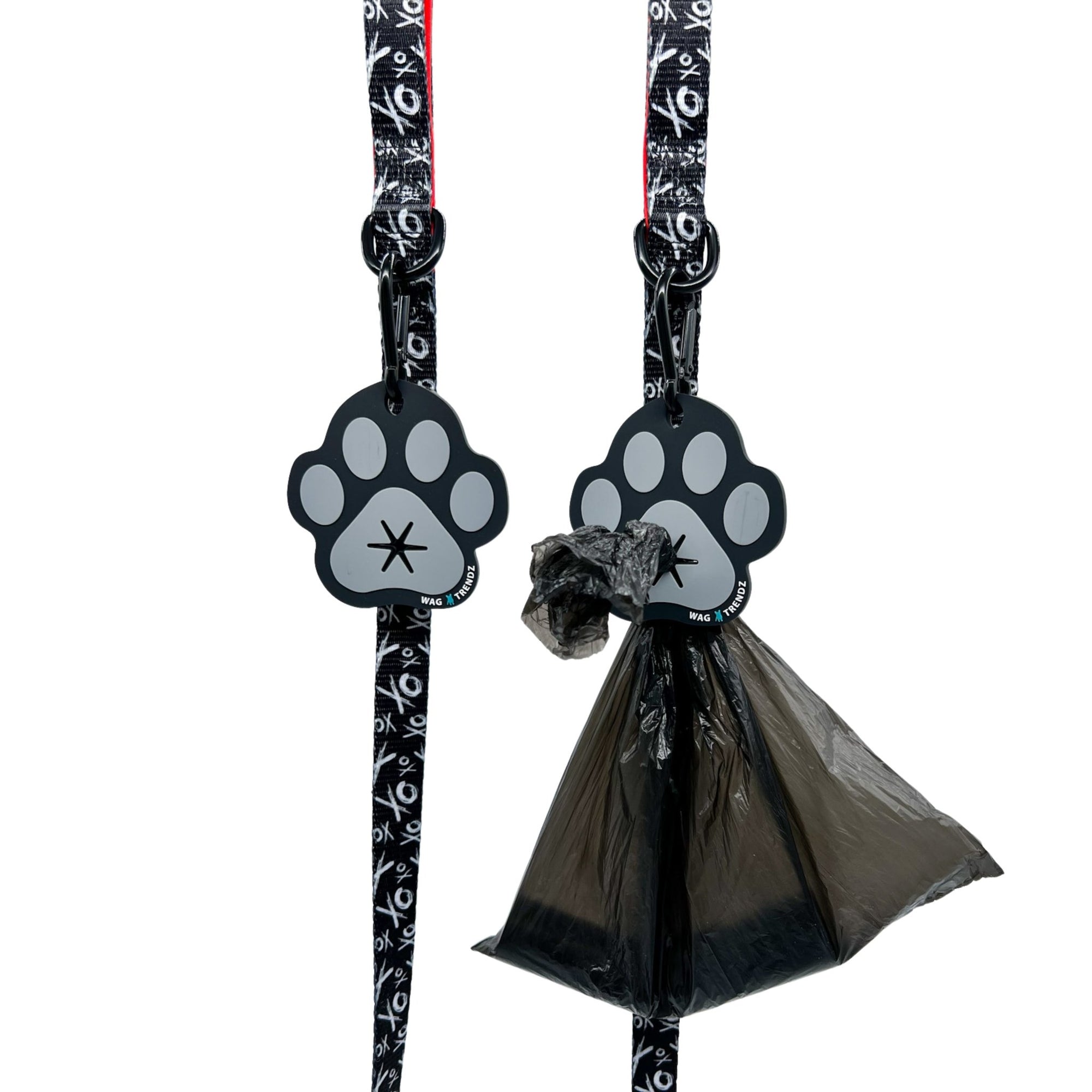 Poop Buddy - black and gray resin dog paw - two hanging on two black &amp; white dog leashes XO with red accents and black plastic bag carrying poop pushed through hole on one - against white background - Wag Trendz